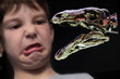 Reflection of a boy pulling funny face at a dinosaur on a tablet computer