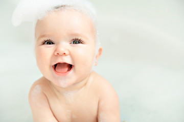a baby girl bathes in a bath with foam and soap bubbles