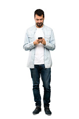 Wall Mural - Full-length shot of Handsome man with beard sending a message with the mobile over isolated white background