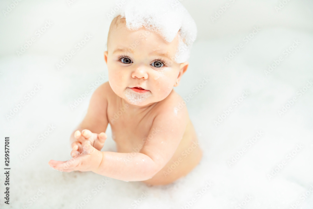 A Baby girl bathes in a bath with foam and soap bubbles - obrazy, fototapety, plakaty 