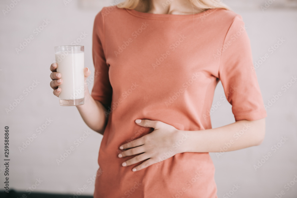 cropped view of woman holding glass of milk while having stomach ache - obrazy, fototapety, plakaty 