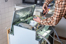 People In Technician Jobs. Appliance Repair Technician Or Handyman Works On Broken Dishwasher In A Kittchen. Laborer Is Changing The Heating Element.