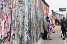 Close-up Of Graffiti At The East Side Gallery, Section Of The Berlin Wall In Berlin, Germany. Street Musician And Tourists In The Background.