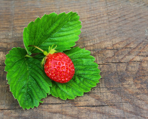 Bright ripe strawberries lying on a wooden table with green leaves. Close up view from top.