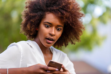 Canvas Print - Outdoor portrait of a Young black African American young woman texting  on mobile phone