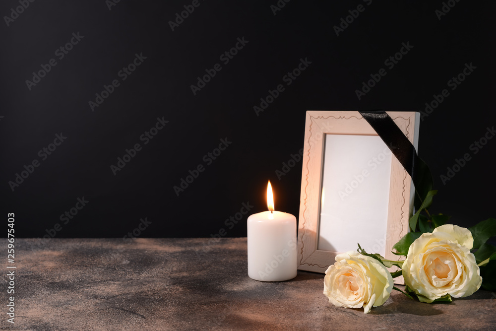 Blank funeral frame, candle and flowers on table against black background