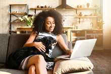 Beautiful African-American Woman With Cute Dog Working On Laptop At Home