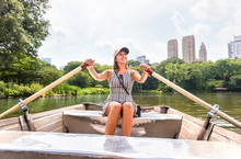Woman rowing a rowboat and having fun in nature. Boating in summer. Smiling happy lady enjoying outdoor activity. Girl on row boat in Central Park, New York. Wanderlust, freedom and healthy lifestyle.
