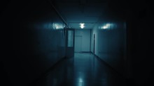 Tracking Inside A Long Dark Gloomy Corridor. A Dark Silhouette Of A Girl Dressed In A Parka Stops In Front Of The Camera.White Big Clocks Hang On The Wall And Show Ten To Eleven.Concept Of Horror.