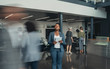 © JonoErasmus - Beautiful black african business woman standing in a busy lobby of an office looking upwards, holding a tablet with people walking past in a blur