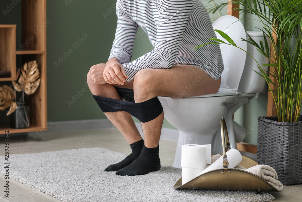 Man sitting on toilet bowl at home