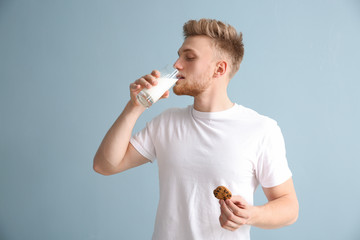 Wall Mural - Handsome young man with tasty cookie drinking milk on color background