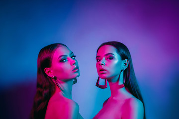 Wall Mural - High fashion models in colorful bright neon lights posing at studio. Portrait of beautiful girls with trendy glowing make-up. Art design vivid style.