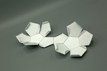 Wall Mural - Geometric shape cut out of paper and photographed on grey background.Dodecahedron. 2d shape foldable to form a 3d shape or a solid.