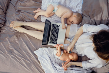 Young beautiful mother freelancer with two children working on a laptop. Freelance, work at home