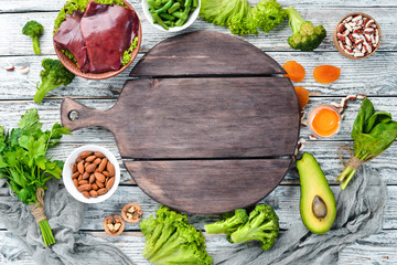 Food containing natural iron. Fe: Liver, avocado, broccoli, spinach, parsley, beans, nuts, on a white wooden background. Top view.