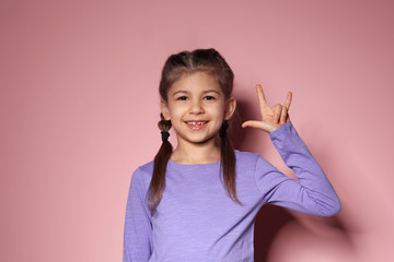 Little girl showing I LOVE YOU gesture in sign language on color background