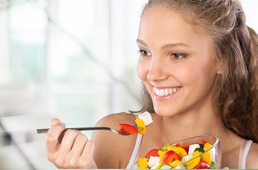 Wall Mural - Young woman eating fruits from glass on blurred background