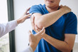 © Ngampol - Doctor physiotherapist assisting a male patient while giving exercising treatment massaging the arm of patient in a physio room, rehabilitation physiotherapy concept