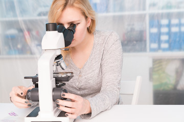 Wall Mural - Young woman medical researcher looking through microscop on slide