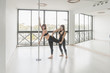 © Alvaro Hernandez/ADDICTIVE STOCK - Side view of young sportive trainer helping lady to stretch leg near pole in light room with big mirror
