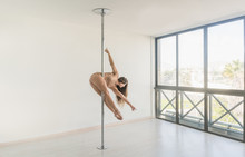 Young Slim Strong Woman Practicing On Pole In Light Room Studio