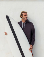 Handsome Adult Guy In Sweater Standing With Craft Surf Board Near White Wall