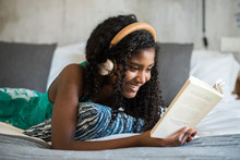 Beautiful Happy Black Teenage Girl With Headphones On Bed Reading A Book