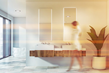 Woman in white bathroom, sinks and tub