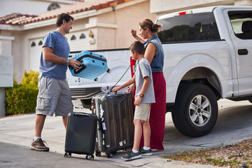 hispanic family packing luggage into pickup truck in front of house