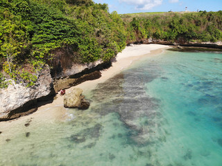 Aerial view of an amazing nature scenery with rock cliff on sandy coastline. Beautiful sea water with waves for surfing in summer season in Bali. Beauty Indian ocean landscape, holiday destination