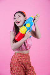 A woman dressed in a traditional Thai folk clothes holding a water gun on a pink background.