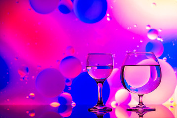 transparent glasses with water and oily drops on colorful background 