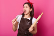 © sementsova321 - Happy singing baker wears kitchen apron smeared with flour, white t shirt, red headband, holds baking rolling pin and whisk. Studio picture isolated over pink background. Cooking skills concept.