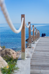 Wooden path to beach with two lonely people under the blue sky