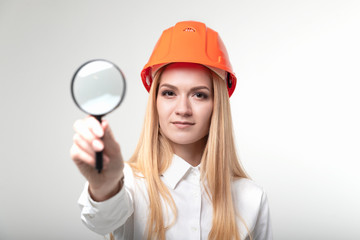 Girl engineer in a protective helmet with a magnifying lens