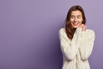 cheerful caucasian girl keeps hands together near face, looks positively aside, has no make up, heal