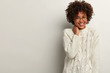 © wayhome.studio  - Glad laughing curly woman giggles as heard funny joke, wears white sweater, keeps hand on neck, expresses positive emotions, stands indoor, blank space right for your advertisement. Happiness