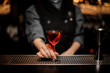 Bartender girl serving a transparent red cocktail in the glass decorated with a lemon zest on the steel bar counter