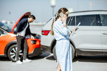 Woman Calling Road Assistance Or Insurance Company Standing On The Road After The Car Collision, Man Checking The Damage