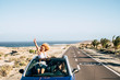 © simona - Happy cheerful couple of young caucasian crazy woman with curly hair enjoy the travel and vacation staying outside the roof of a convertible car with long road and ocean in background - joyful