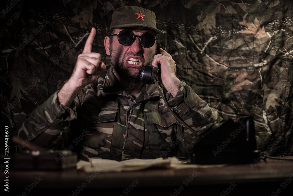 The evil dictator sitting on table. Angry communist general sitting at headquarter or Cuban commander in dark room. - obrazy, fototapety, plakaty 