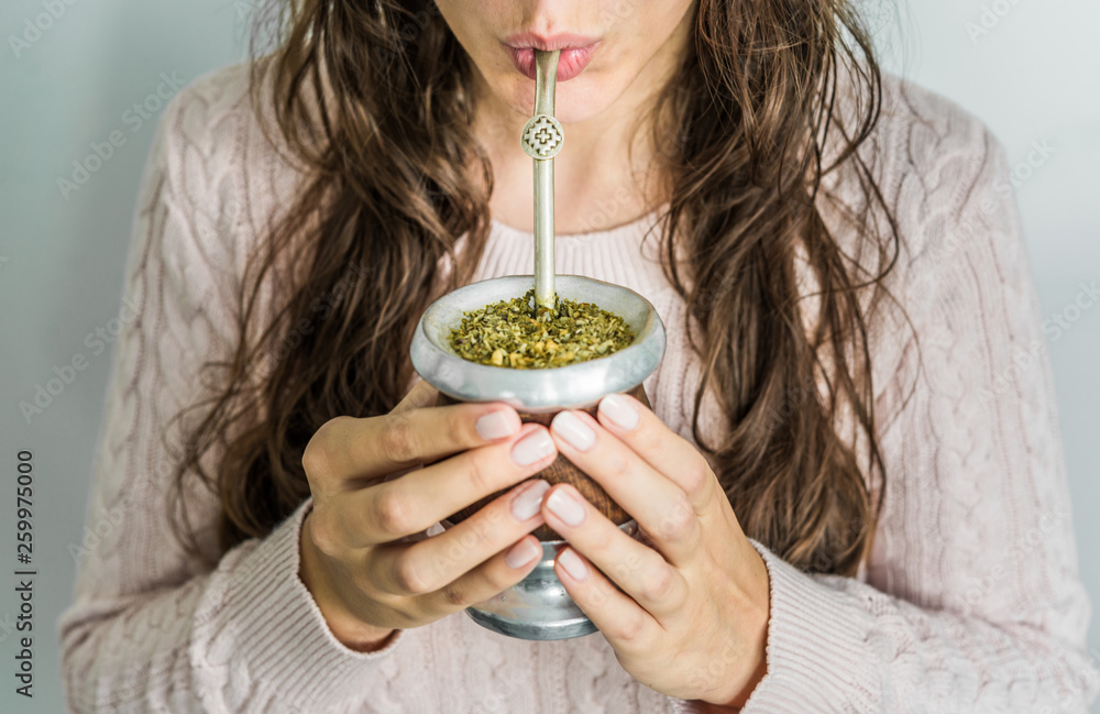 Young woman drinking traditional Argentinian yerba mate tea from a calabash gourd with bombilla stick  - obrazy, fototapety, plakaty 