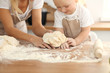 © rogerphoto - Little girl and her blonde mom in beige aprons  playing and laughing while kneading the dough in kitchen. Homemade pastry for bread, pizza or bake cookies. Family fun and cooking concept