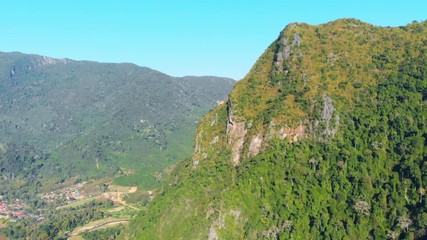 Wall Mural - Aerial: drone flying over natural rainforest green jungle populating steep valley cliffs in the mountains of North Laos, travel destination in South East Asia.