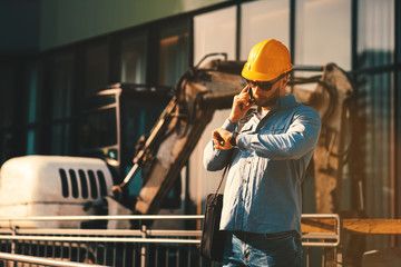 Construction engineer talking on the phone and looking at the watch on the construction site