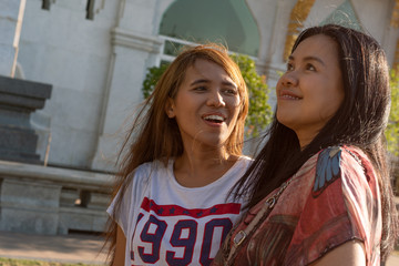 Asian mother and daughter smiling and laughing together in bright sunlight outdoors - Two happy ethnic females enjoying time together in a park