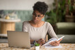 © fizkes - Focused african student looking at laptop holding book doing research