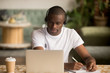 © fizkes - African man wearing headphones watching webinar making notes study online