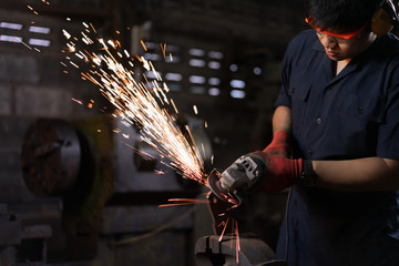 Asian male workshop engineer operating an angle grinder on a metal part with sparks flying - Hispanic repair man using power tools wearing safety equipment in repair shop